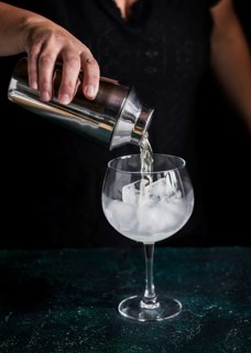 A bartender skillfully pours a refreshing gin tonic from a shaker into a glass filled with large