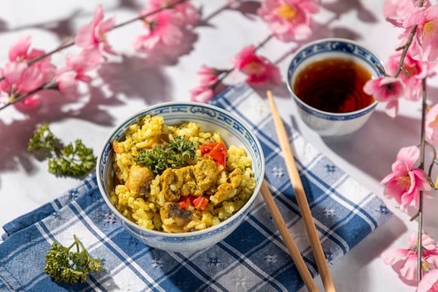 Chinese bowl with rice and vegetables next to tea, decorated with cherry blossoms