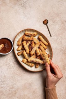 From above cropped unrecognizable hand holding an homemade churros dusted with sugar and cinnamon,