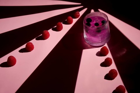 A striking composition featuring a pink drink garnished with berries alongside a row of fresh
