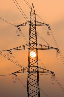 Setting sun behind silhouette of high-voltage power line pylons, shrouded in orange light amidst