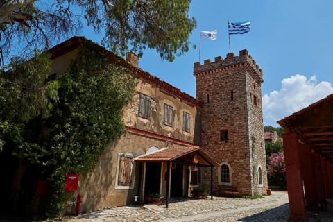 A historic building with a tower surrounded by trees and two flags, Achaia Clauss Winery, Patras,