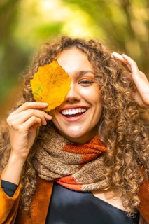 Vertical autumn portrait of a smiling woman with curly hair hiding on a leaf