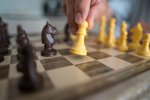 Cropped unrecognizable elderly person holding a chess piece, focusing on an intense game strategy.