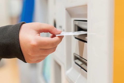 A passenger processes travel documents using an airport check-in kiosk. The close-up image
