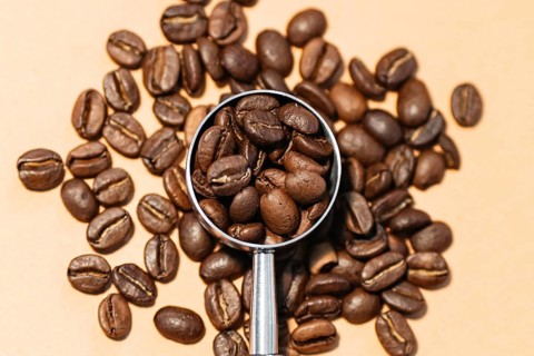 A close up view of roasted coffee beans scattered on a surface, with a metallic scoop in the center