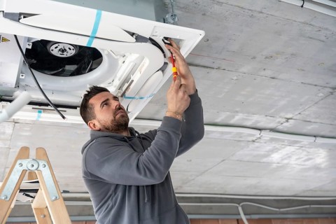 Professional hvac technician standing on a ladder and using a screwdriver to install a new air