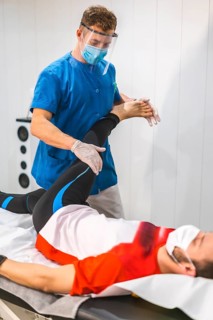 A physiotherapist with mask working with a patient. Physiotherapy with protective measures for the