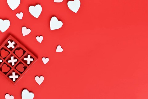 Valentine-themed heart game with red hearts and white Xs in a red box on a red background with copy