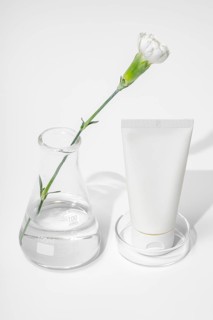 A modern skin care laboratory setup with a white flower stem extending through a clear flask and a