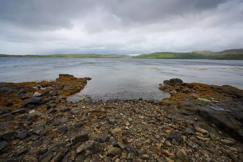 A rocky beach overlooking a murky lake under grey clouds, Portnalong, Isle of Skye, Scotland,