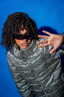 Young woman with curly hair wearing stylish sunglasses and animal print jacket making a hand