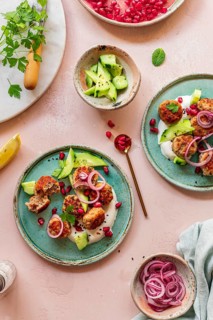 A vibrant Mediterranean dish featuring meatballs, fresh cucumbers, yogurt, pomegranate seeds, and