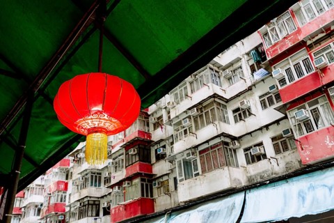 A bright red Chinese lantern hangs under a green awning, set against the densely packed, weathered