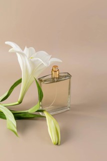 Elegant perfume bottle with a golden cap sits beside delicate white lily flowers on a soft beige