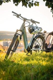 E-bike with helmet and trailer standing in the grass with a wide view in the background, e-bike,
