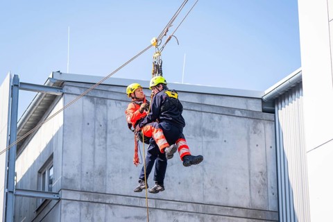 Two workers wearing protective clothing carry out a rescue exercise on a concrete building, Opening