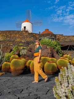 A woman strolls near a traditional windmill surrounded by cacti in Lanzarote, Canary Islands,