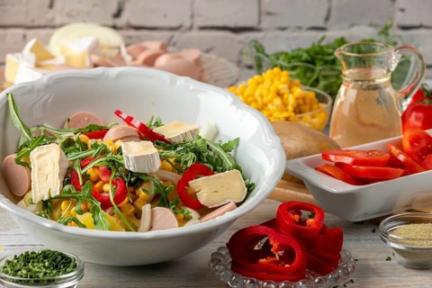 Potato salad with camembert, sausage and fresh arugula, surrounded by other ingredients