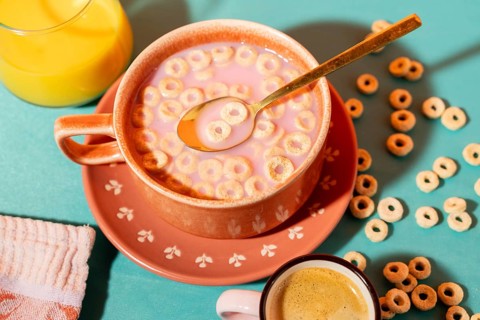 Top view of a colorful breakfast setting featuring a ceramic bowl of cereal with milk, a cup of