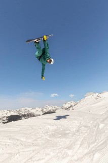 A snowboarder dressed in green gear gracefully executes a dynamic jump against a backdrop of
