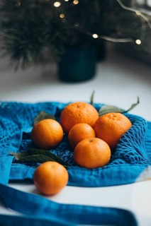 Luscious tangerines nestled in a vibrant blue string bag, contrasted by soft holiday lights in the