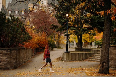 Side view of unrecognizable redhead woman walking through a vibrant autumn scene in Montreal. The