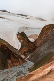 Steaming stream between colourful rhyolite mountains and snowfields, Hveradalir geothermal area,