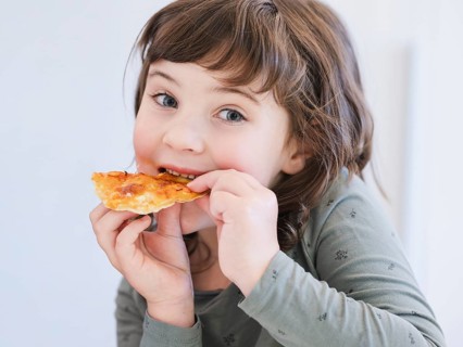 A young child joyfully eats a slice of pizza, showcasing the simple delights of childhood. The
