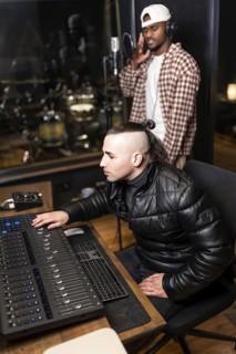 Sound engineer using mixing console while singer recording new pop album in professional music