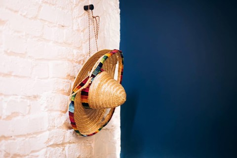 A traditional woven sombrero with colorful, vibrant trim hangs on a rustic white brick wall against