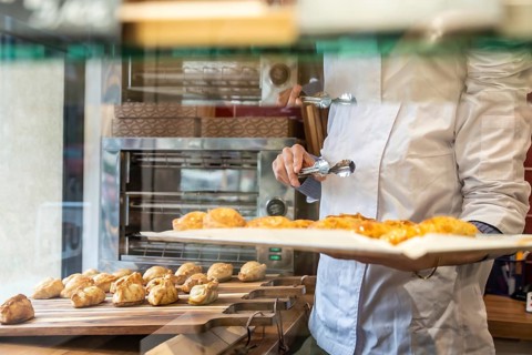 Chef wearing a white uniform holding a tray with freshly baked pastries, using tongs to move sweet