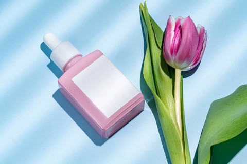 Top view of a pink cosmetic dropper bottle alongside a beautiful pink tulip, presented on a