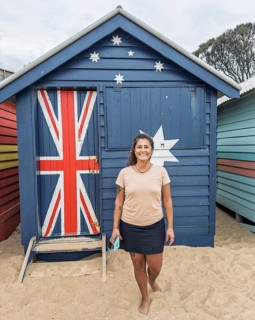 A cheerful tourist stands in front of a vibrant Brighton Beach hut in Melbourne, Australia. The