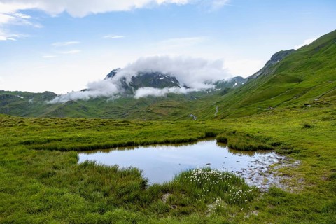 Mountain landscape and small pond, clouds moving around mountain peaks, Grindelwald First, Bernese