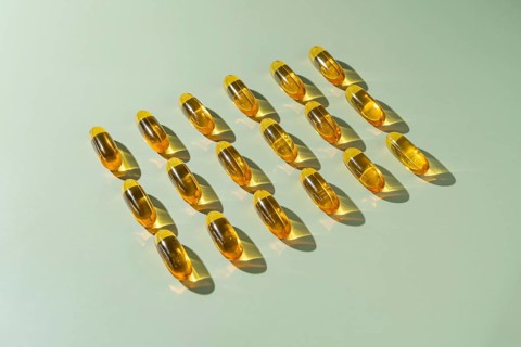 From above multiple omega 3 fish oil capsules neatly aligned in rows on a light green background,