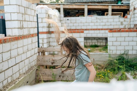 A young girl is joyfully playing amidst the unfinished structures at a construction site, her hair