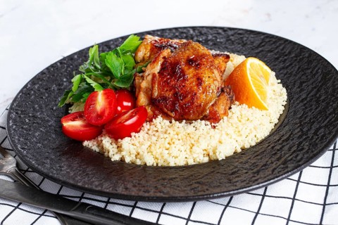 Grilled chicken served with couscous with fresh vegetables and herbs on a black platter, Greek