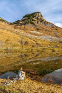 Lake Augstsee and the Atterkogel mountain on the Loser. A hiker sits on a rock. Autumn, good