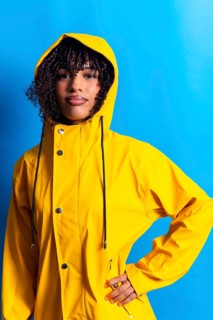 Studio portrait of a young woman wearing a yellow raincoat, posing against a vibrant blue