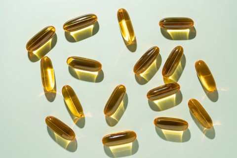 Top view of golden Omega 3 capsules cast in soft shadows on a pale green background, illustrating a