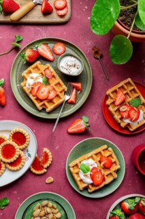 A rustic breakfast scene with homemade waffles topped with fresh strawberries and creamy yoghurt.