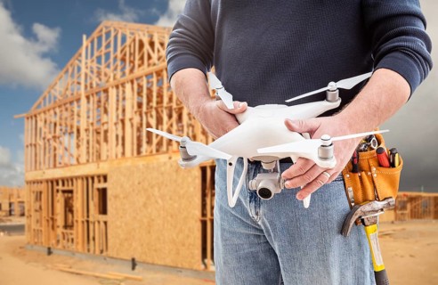 Construction Worker and Drone Pilot With Toolbelt Holding Drone At Construction Site