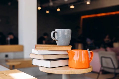 A cozy cafe scene featuring a stack of books on a wooden table, accompanied by a gray mug and a