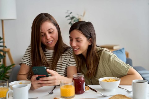 A lesbian couple shares a warm moment at breakfast, smiling as they look at a phone together The