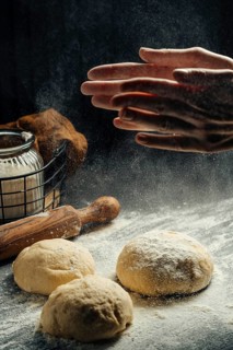 A pair of hands dusts flour over dough balls in a rustic kitchen, ready for baking. A rolling pin,