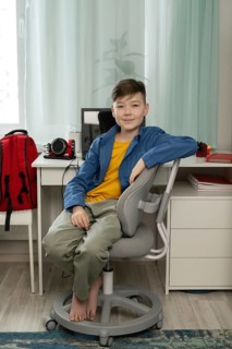 A young boy sits comfortably on a chair in a modern study room with a desk, computer, and red