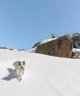 A snowboarder sits at the edge of a rocky cliff, observing the snowy environment as an energetic