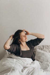 A woman in casual wear sits comfortably on a bed, savoring a serene morning moment. Her relaxed