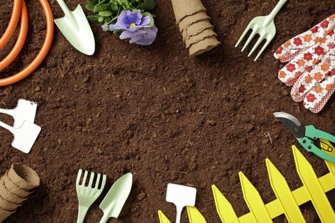 A variety of garden tools and accessories like gloves, pots, and a hose rest on fresh soil, ready